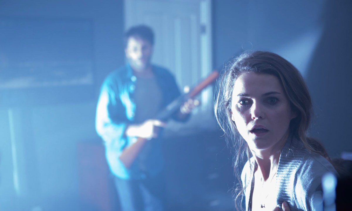A woman in the dark looking scared, a man in the background with a rifle in Dark Skies.